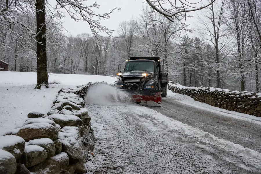 Snow plow clearing a gravel driveway lined with stone walls in rural Connecticut