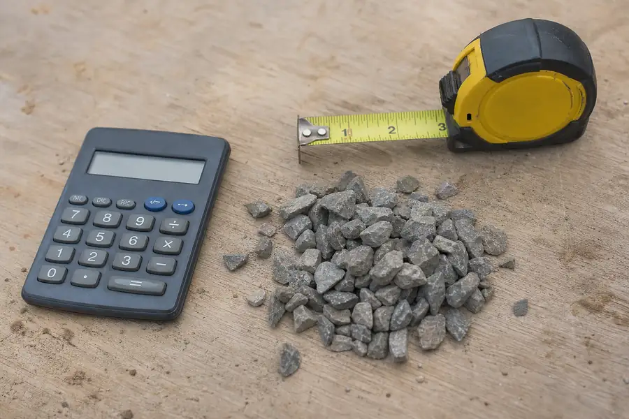 Calculator, tape measure and a handful of crushed stone on a workbench