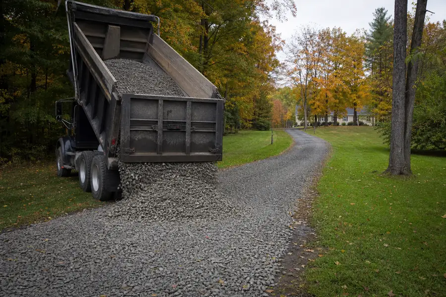 Dump truck delivering gravel to a long driveway on a Connecticut property in autumn