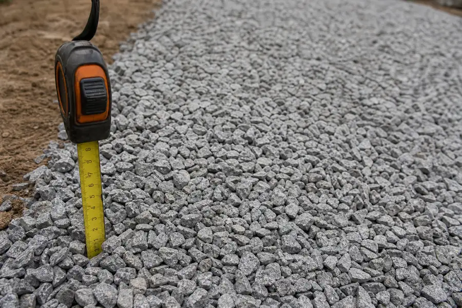 Tape measure held against a freshly spread layer of crushed stone