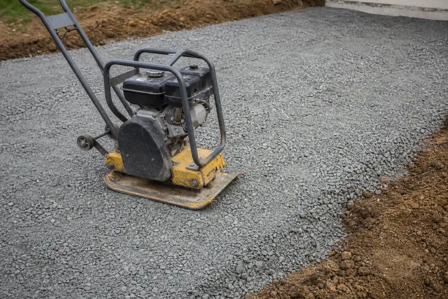 Plate compactor packing a layer of gray processed gravel on a fresh driveway